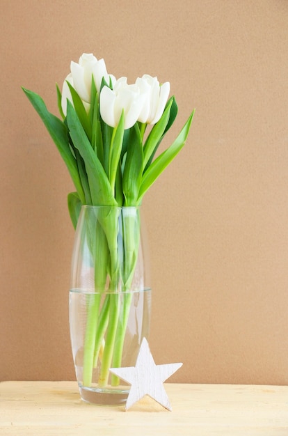 Tulipas brancas em um vaso de vidro sobre uma mesa de madeira