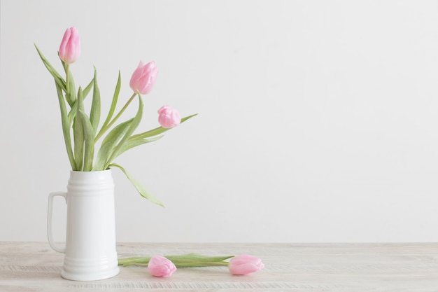 Tulipas cor de rosa no jarro de cerâmico branco na mesa de madeira na parede do fundo branco