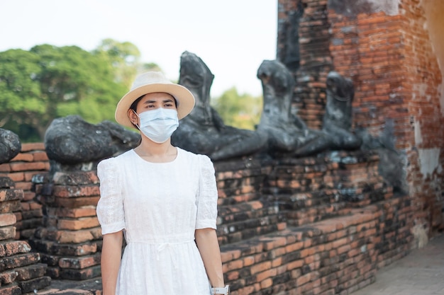 Foto turista usando máscara cirúrgica visitando o templo wat chaiwatthanaram