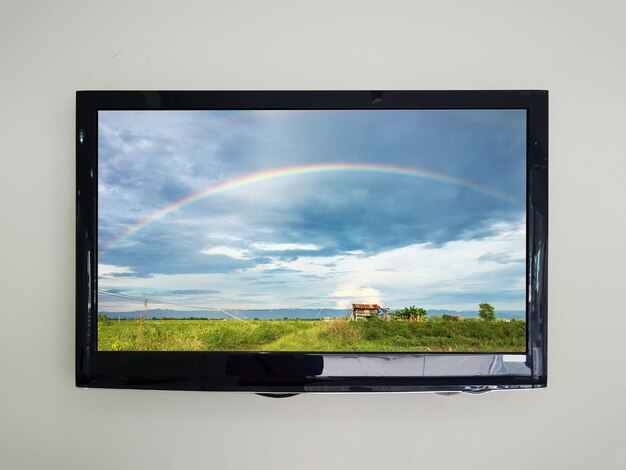 Foto tv led no fundo da parede com arco-íris no céu sobre o campo de agricultura na tela da televisão