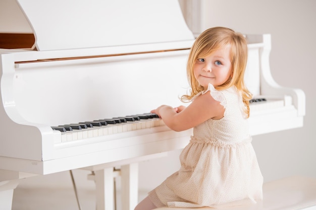 Um bebê toca um grande piano branco em uma sala ensolarada