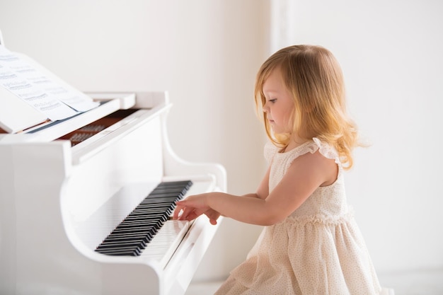 Um bebê toca um grande piano branco em uma sala ensolarada