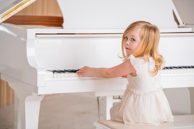 Um bebê toca um grande piano branco em uma sala ensolarada