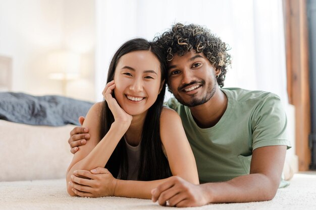 Foto um casal multi-racial feliz relaxando e sorrindo em casa juntos abraçando-se olhando para a câmera