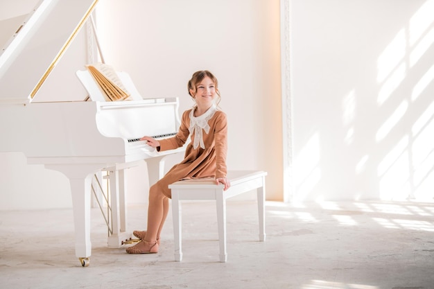 Uma garotinha toca um grande piano branco em uma sala ensolarada