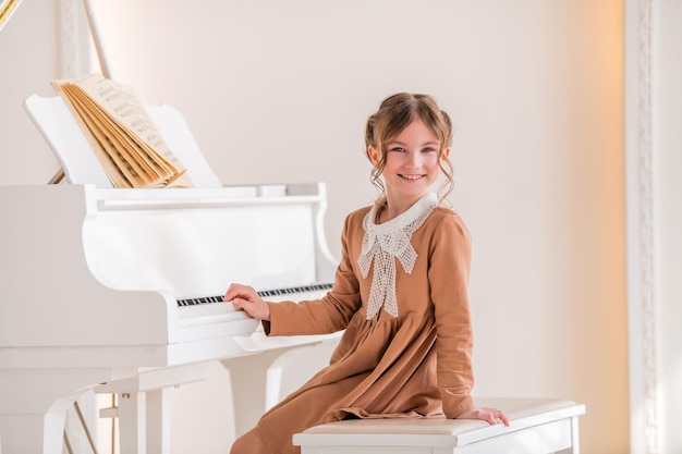 Uma garotinha toca um grande piano branco em uma sala ensolarada