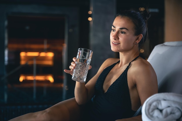 Uma jovem com um copo de água depois da sauna está descansando