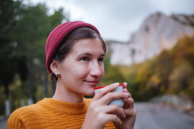 Uma jovem turista bebe uma bebida quente de uma xícara e aprecia a paisagem nas montanhas