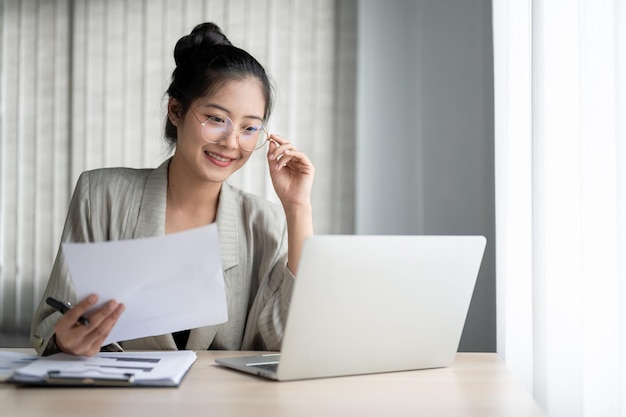 Foto uma linda empresária está tocando seus óculos enquanto lê um relatório on-line em seu laptop