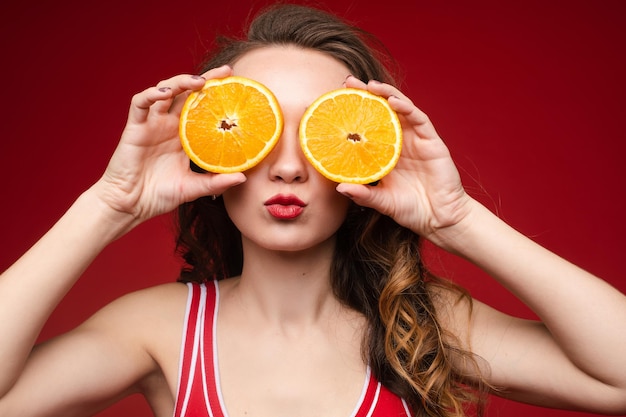 Uma linda mulher de maiô vermelho com laranjas nas mãos está se divertindo no verão O conceito de recreação