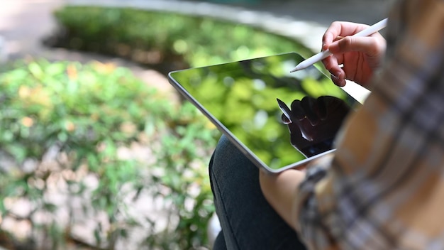 Uma mulher anotando suas ideias de projeto no touchpad do tablet enquanto relaxa no parque