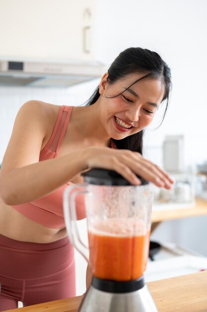 Uma mulher asiática atraente e saudável em roupas esportivas fazendo um smoothie na cozinha com um liquidificador