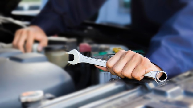 Foto uma pessoa segurando uma chave inglesa que está sendo usada para consertar um motor de carro