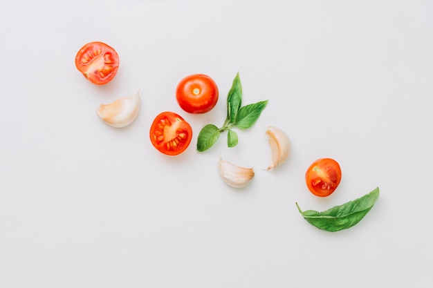 Uma visão aérea de tomates cereja cortados ao meio e inteiros; alho, cravo, e, manjericão, folha, branco, fundo