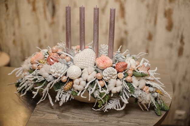 Vaso de cor branca com uma composição de decoração de Natal de galhos de pinheiro, velas, flores e enfeites na mesa