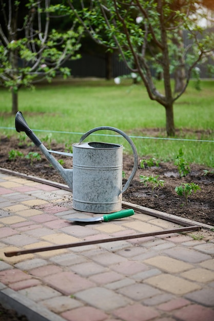 Velho regador de metal e pá de jardinagem em pedras de pavimentação contra o pano de fundo de um jardim