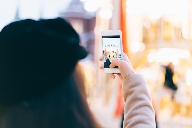 Visão traseira da mulher desfocada usando telefone celular e tirando foto de merrygoround no recinto de feiras da cidade