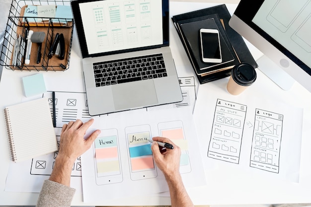 Foto vista acima do designer da interface do aplicativo fazendo anotações sobre o esquema enquanto planeja o design do menu no escritório