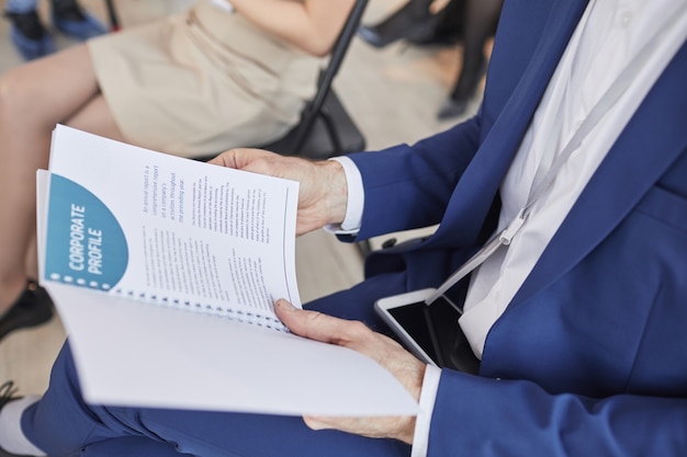 Vista lateral recortada de um homem irreconhecível segurando o planejador de folheto do Projeto enquanto está sentado na platéia em uma conferência de negócios, copie o espaço