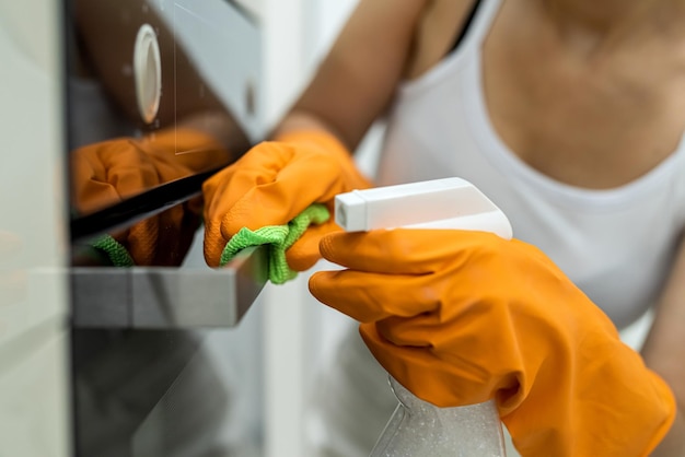 Weibliche Hände in Handschuhen mit einer Flasche Reinigungsmittel, die Küchenofen reinigen