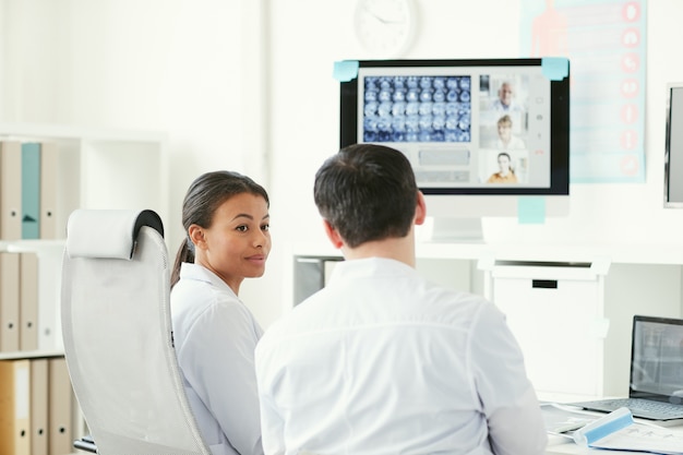 Zwei Ärzte sprechen miteinander, während sie am Tisch sitzen und Röntgenbilder im Büro untersuchen