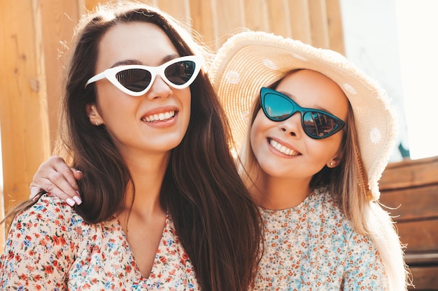 Zwei junge schöne lächelnde Hipster-Frauen in trendiger SommerkleidungSexy sorglose Frauen posieren auf dem Straßenhintergrund mit Hut Positive reine Modelle, die sich bei Sonnenuntergang amüsieren und sich umarmen Fröhlich und fröhlich