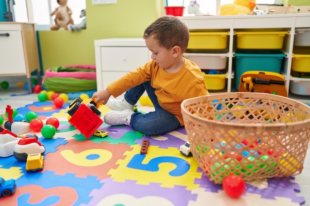 Free Photo adorable caucasian boy playing with tractor toy sitting on floor at kindergarten