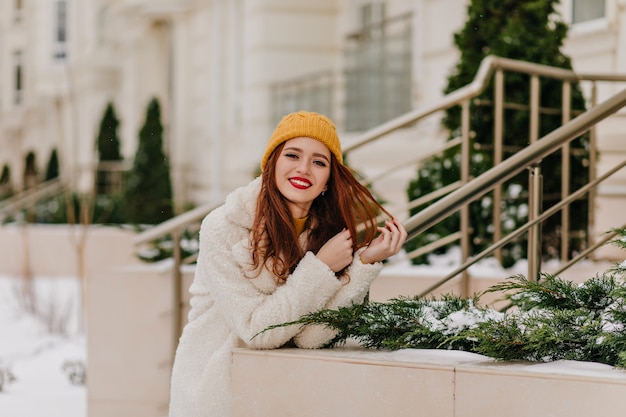 Free photo adorable ginger girl in hat expressing positive emotions. gorgeous female model relaxing in winter.