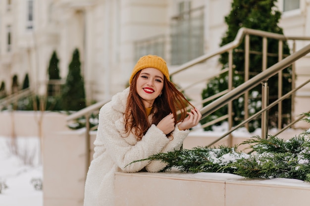 Adorable ginger girl in hat expressing positive emotions. Gorgeous female model relaxing in winter.