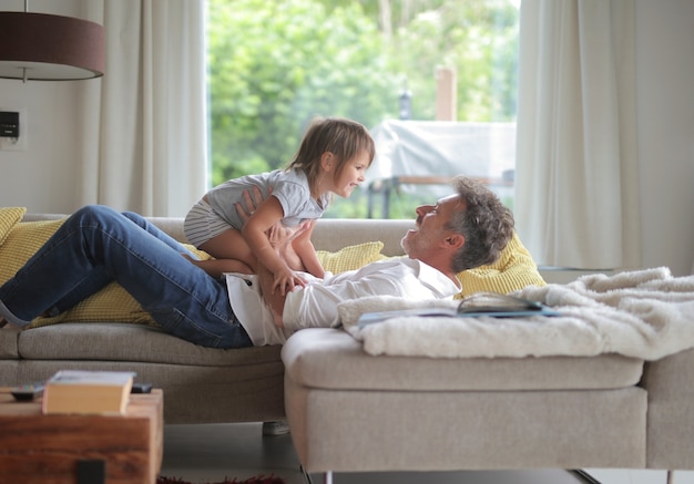 Free photo adult male lying on the sofa and playing with his child under the sunlight through the windows