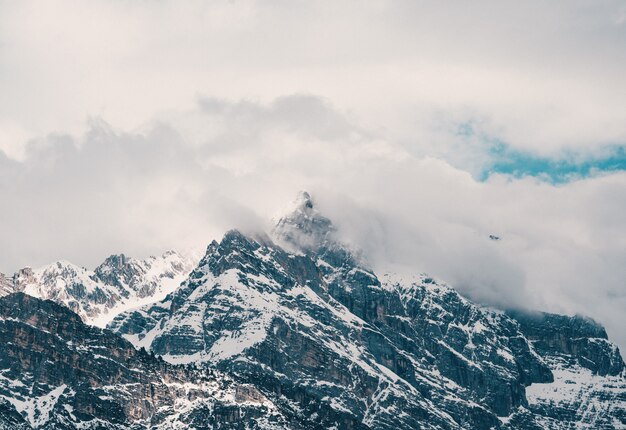 Aerial shot of beautiful rocky snowy mountains covered in clouds