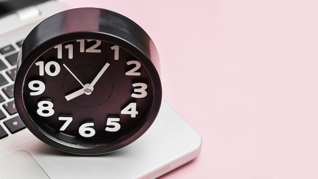 Alarm clock on laptop against pink background