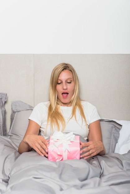 Free photo amazed woman in bed with gift box