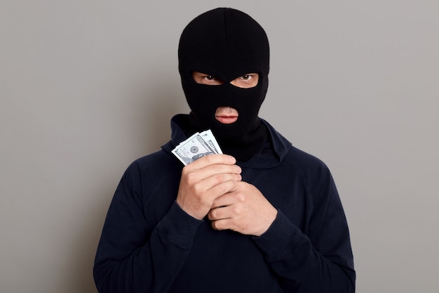 Free Photo angry burglar guy looks at the front with a forged expression and holds the stolen money in his hands