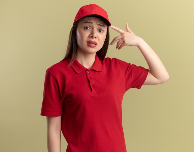 Free Photo anxious pretty delivery woman in uniform points at cap on olive green