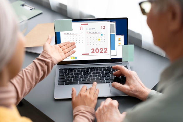 Arabic woman teaching senior man to use calendar laptop sitting at desk