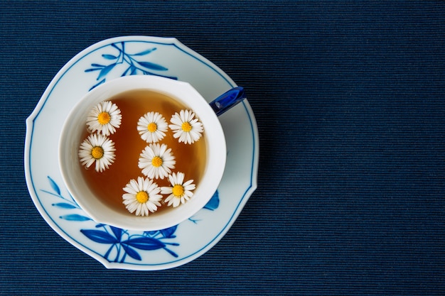 Free photo aromatic chamomile tea in a cup and sauce on a dark placemat background. flat lay.