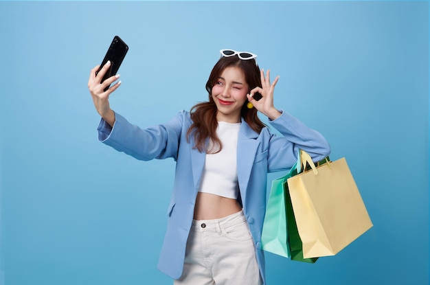 Free photo asian shopper woman holding shopping bag and using mobile phone shooting selfie