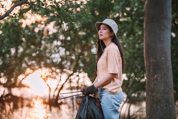 Бесплатное фото Азиатская женщина-волонтер по охране окружающей среды собирает пластиковый и пенопластовый мусор в мешок для мусора в общественном паркеvvolunteering save world concept
