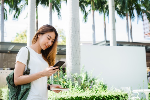 Free photo asian woman tourist backpacker smiling and using smartphone traveling alone