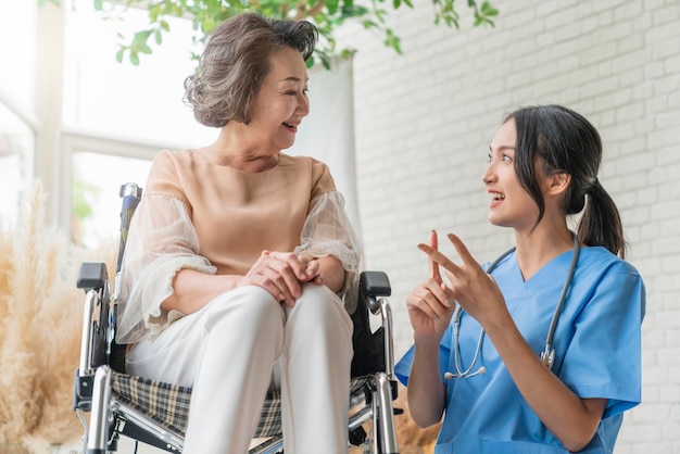 Free photo asian young caregiver caring for her elderly patient at senior daycare handicap patient in a wheelchair at the hospital talking to a friendly nurse and looking cheerful nurse wheeling senior patient