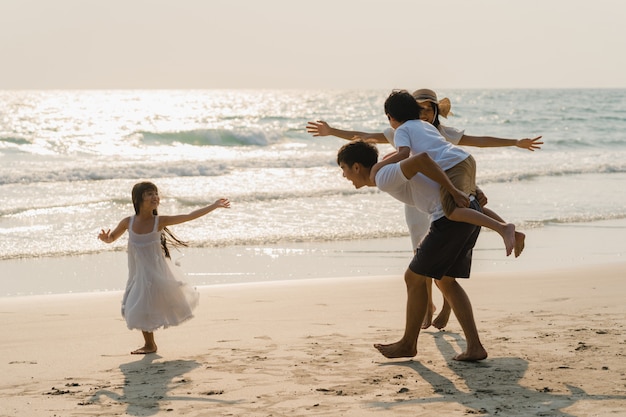 Free photo asian young happy family enjoy vacation on beach in the evening. dad, mom and kid relax playing together near sea when sunset while travel holiday. lifestyle travel holiday vacation summer concept.