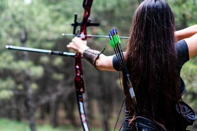 Free photo athletic female aiming with bow and arrow towards the trees