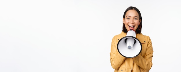 Foto gratuita annuncio di attenzione immagine di una donna asiatica che grida nel megafono che recluta cercando persone che condividono informazioni in piedi su sfondo bianco