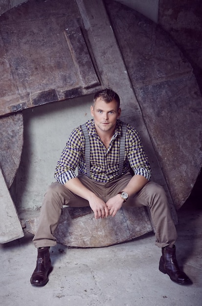 Free photo attractive brutal man in checkered shirt posing in a room of a warehouse.