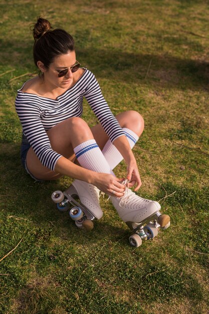 An attractive young woman sitting on green grass tying the lace of roller skate