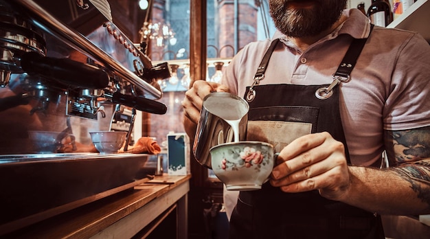 Free photo barista in apron making a cappuccino, pouring milk in a cup in a restaurant or coffee shop