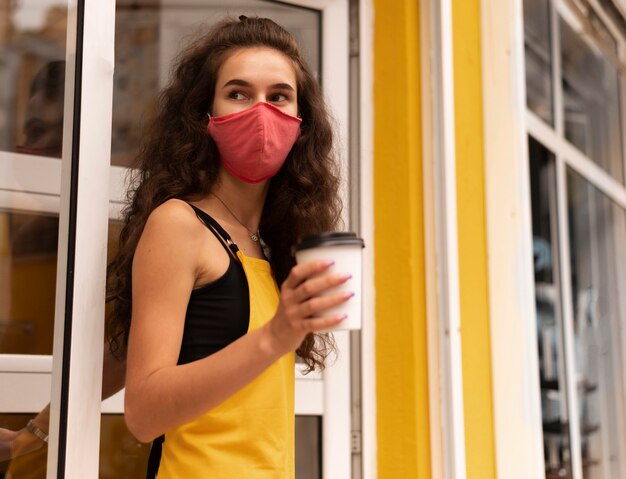 Free photo barista wearing a face mask while holding a cup of coffee outdoors