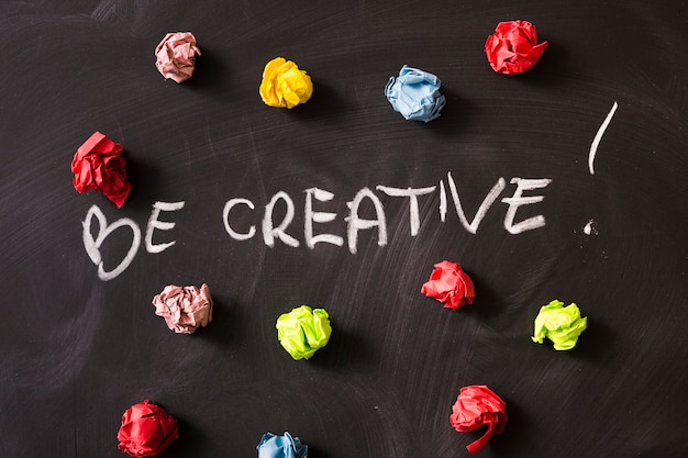 Free photo be creativity word with colorful crumpled paper ball on blackboard