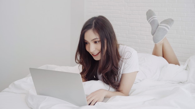 Free Photo beautiful asian mix race caucasian woman using computer or laptop while lying on the bed in her bedroom. 